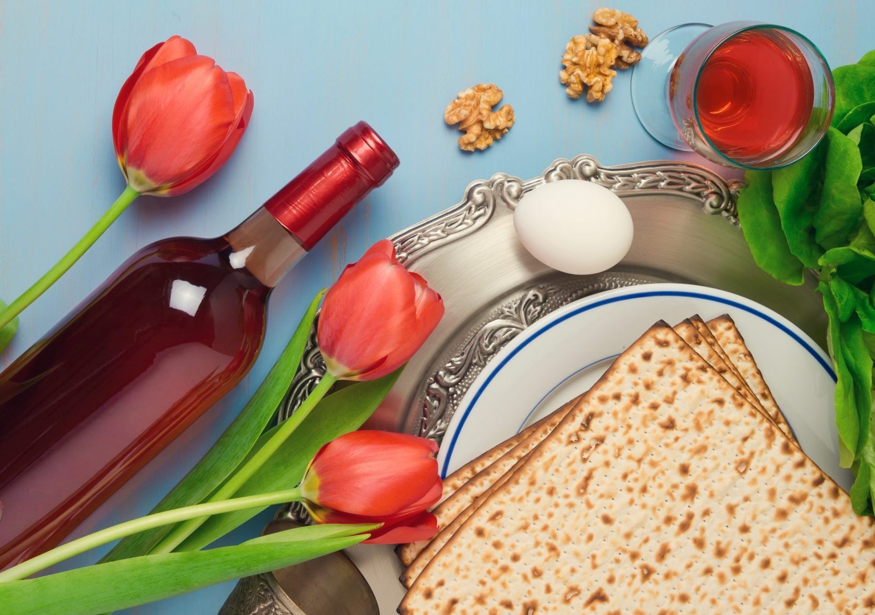 Passover holiday concept seder plate, matzoh and tulip flowers on wooden background. Top view from above
